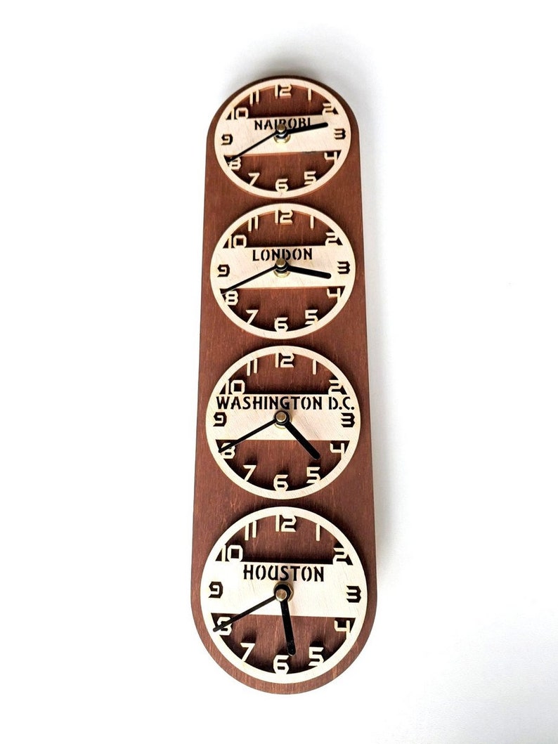 May include: A wooden wall clock with four circular clock faces displaying the time in different cities: Nairobi, London, Washington D.C., and Houston. The clock has a dark brown wooden backing and light-colored clock faces.