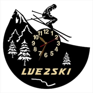 Puede incluir: Reloj de pared negro y blanco con una silueta de esquiador y una escena de monta&ntilde;a. La esfera del reloj tiene n&uacute;meros romanos y una aguja de hora y minutos de color dorado. La esfera del reloj tambi&eacute;n tiene la palabra "LUEZSKI" impresa en dorado.