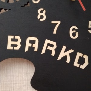 May include: Black wooden clock with gold numbers and a gold metal clock hand. The clock face has the word "BARK" written in gold letters.