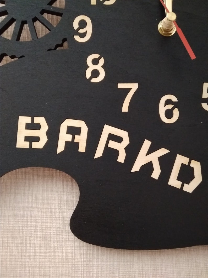 May include: Black wooden clock with gold numbers and a gold metal clock hand. The clock face has the word "BARK" written in gold letters.