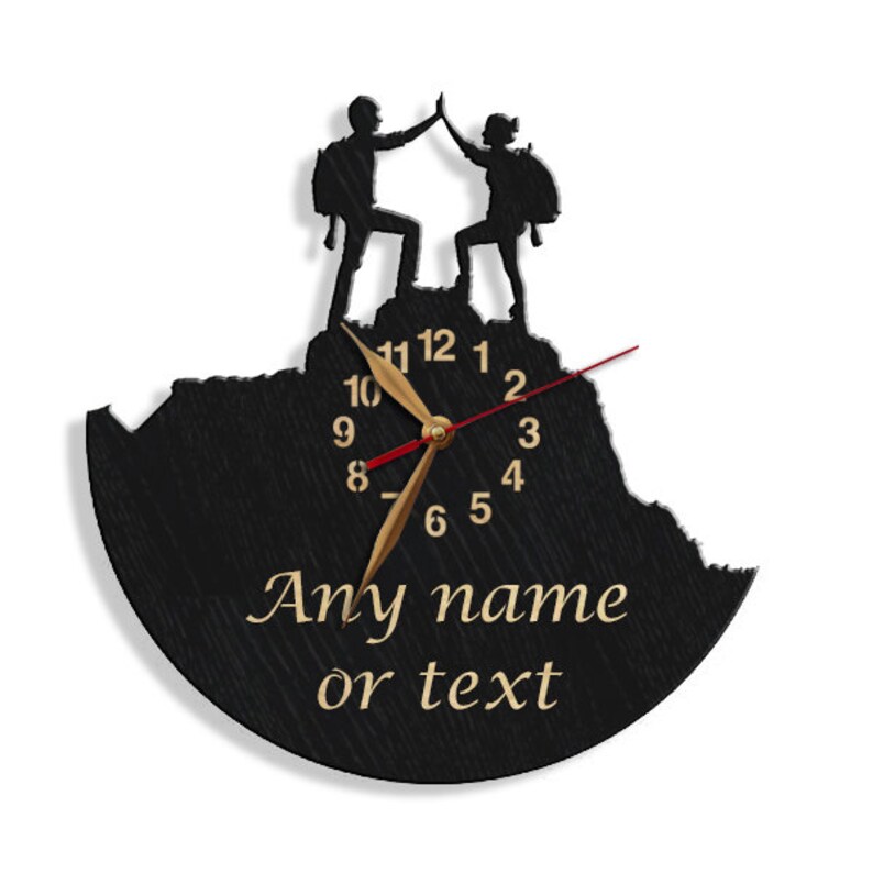 May include: Black wooden clock with a silhouette of two people high-fiving on a mountain top. The clock face has gold hands and black numbers. The text "Any name or text" is printed below the clock face.