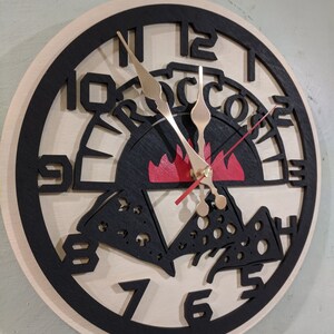 May include: A black and white wooden clock with a pizza design. The clock face has black Roman numerals and a red flame in the center. The words "Pizza" are written in a black arch above the flame.