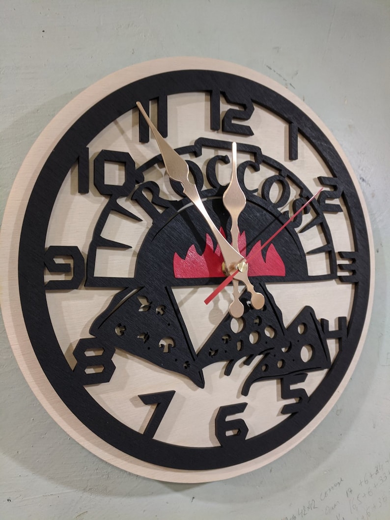 May include: A black and white wooden clock with a pizza design. The clock face has black Roman numerals and a red flame in the center. The words "Pizza" are written in a black arch above the flame.