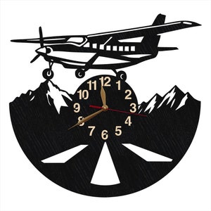 May include: Black and white wall clock with a silhouette of a small airplane flying over mountains. The clock face has a black background with white numbers and a gold hour hand and red minute hand.