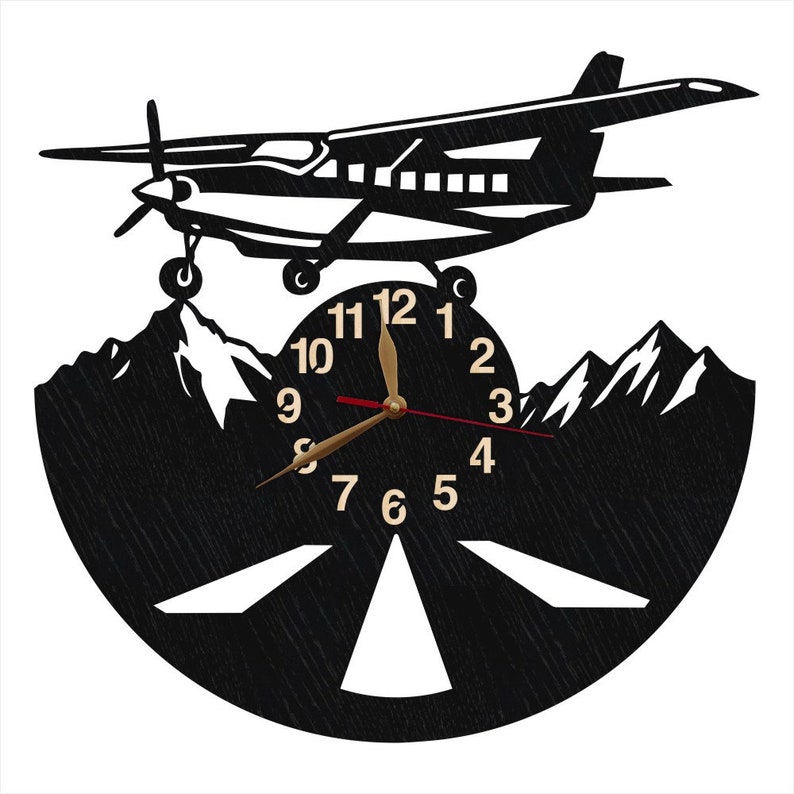 May include: Black and white wall clock with a silhouette of a small airplane flying over mountains. The clock face has a black background with white numbers and a gold hour hand and red minute hand.