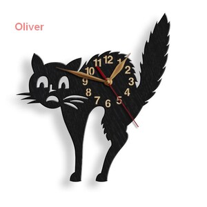 May include: Black silhouette of a cat with a clock face in the center. The clock face has gold numbers and hands. The cat's tail is curled up behind it. The word "Oliver" is written in pink above the cat.