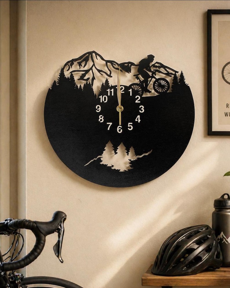 May include: Black metal wall clock featuring a mountain biking scene. The clock has a circular design with a silhouette of a cyclist, trees, and mountains. The clock hands are gold-colored, and the numbers are white.