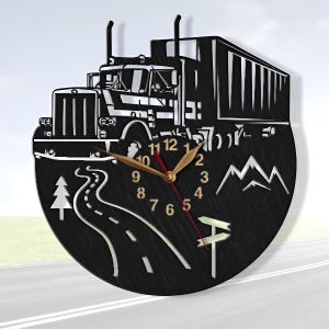 May include: Black and white wall clock with a semi-truck design. The clock features a winding road, mountains, and a pine tree. The clock face has black numbers and gold hands.
