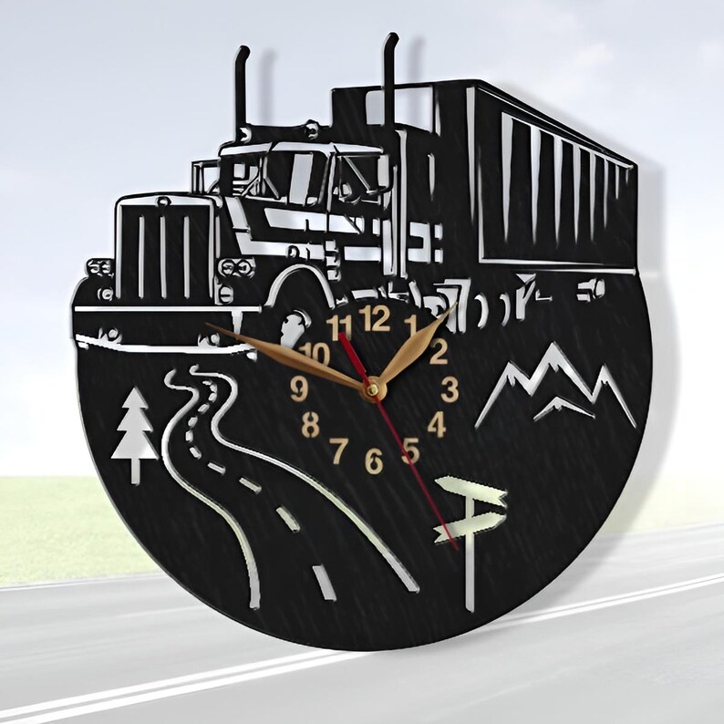 May include: Black and white wall clock with a semi-truck design. The clock features a winding road, mountains, and a pine tree. The clock face has black numbers and gold hands.