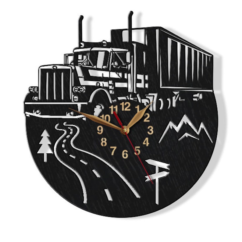May include: Black and white wall clock featuring a silhouette of a lorry driving along a winding road with mountains in the background. The clock face has gold numbers and hands.