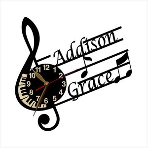Puede incluir: Reloj blanco y negro con un dise&ntilde;o de clave de sol. La esfera del reloj tiene un dise&ntilde;o de teclas de piano y las palabras "Addison Grace" est&aacute;n escritas en la clave de sol.