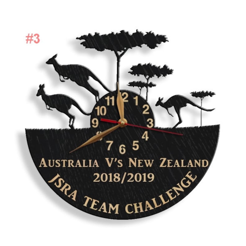 May include: A black wooden clock with a silhouette of kangaroos and trees. The clock face has gold numbers and hands, and the text "AUSTRALIA V'S NEW ZEALAND 2018/2019 ISRA TEAM CHALLENGE" is printed in gold.