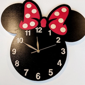 May include: Black wooden clock shaped like a cartoon mouse head with a red bow with white polka dots. The clock face has white numbers 1 through 12 and black hands.