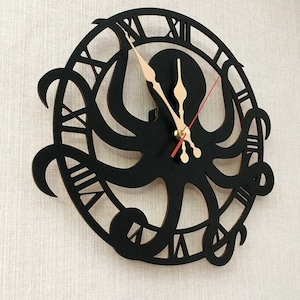 May include: A black octopus wall clock with Roman numerals. The clock has a cut-out design of an octopus in the centre, with the tentacles extending outwards. The clock hands are beige, and the second hand is red. It is mounted on a textured, off-white wall.