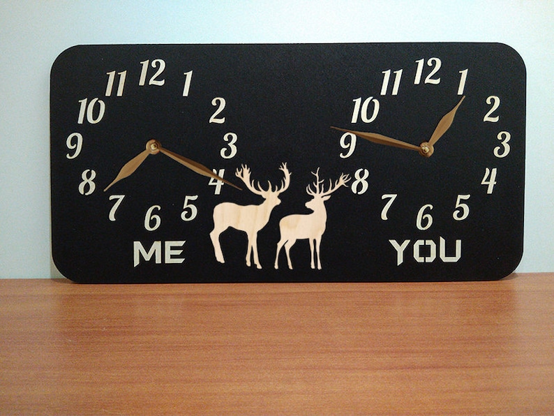 May include: A black wooden clock with two clock faces, one labelled "ME" and the other "YOU". Each clock face has a deer silhouette and gold-coloured hands.