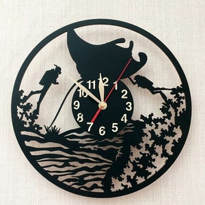 May include: Black and white wall clock with a scuba diving theme. The clock face features a manta ray, two divers, and a coral reef. The numbers 1 through 12 are displayed around the clock face.
