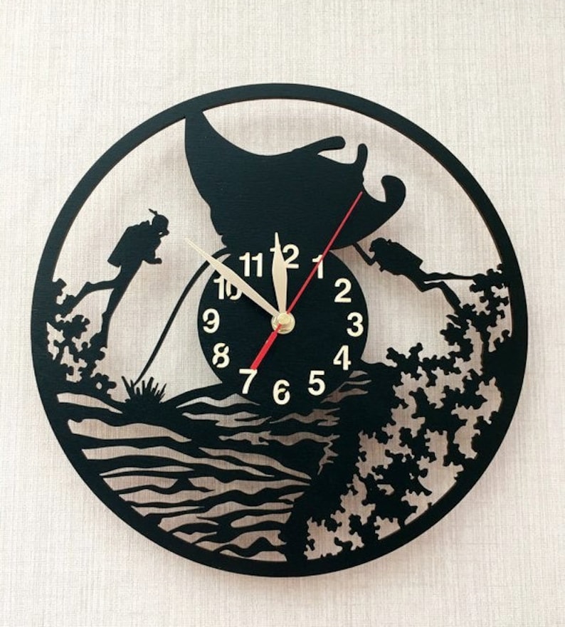 May include: Black and white wall clock with a scuba diving theme. The clock face features a manta ray, two divers, and a coral reef. The numbers 1 through 12 are displayed around the clock face.