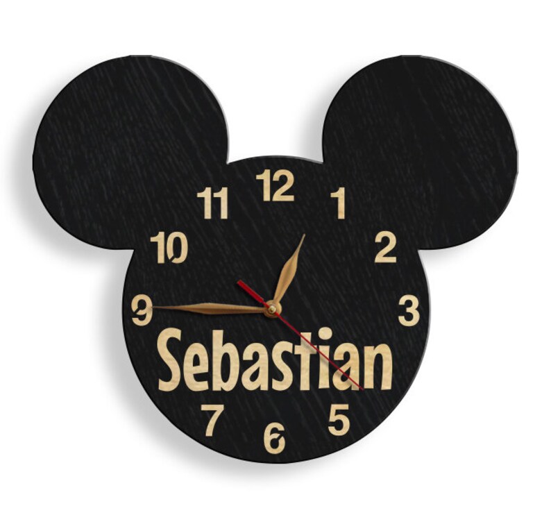 May include: Black wooden Mickey Mouse-shaped clock with gold numbers and hands. The name "Sebastian" is written in gold letters below the clock face.