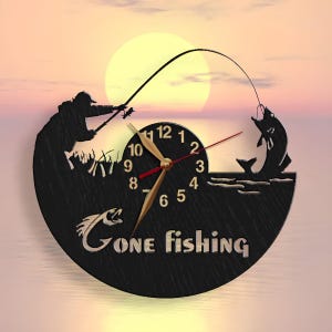 May include: A black wooden clock with a silhouette of a person fishing. The clock face has Roman numerals and the words "Gone Fishing" are printed below the clock face.