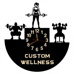 May include: Black and white silhouette of a clock with a custom wellness design. The clock face features a black background with white numbers and gold hands. The clock is surrounded by three silhouettes of people lifting weights.