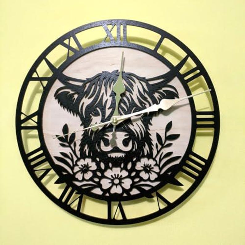 May include: A round wooden wall clock with a black frame and Roman numerals. The clock face features a Highland cow design in black and natural wood tones, with floral accents. The clock hands are gold.
