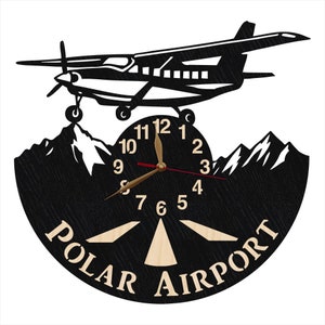May include: Black and white clock with a silhouette of a small plane flying over mountains. The clock face has a wooden runway design and the words "POLAR AIRPORT" printed on the bottom.