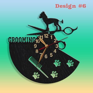 May include: Black wooden clock with a grooming theme. The clock face features a pair of scissors, a comb, and paw prints. The words "Grooming" are displayed at the top of the clock face. The clock hands are gold and red.