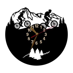 May include: Black wall clock featuring a mountain biking theme. The clock face is black with gold-colored hands and numbers. Silhouettes of cyclists and mountain scenery are incorporated into the design, creating a unique decorative piece.
