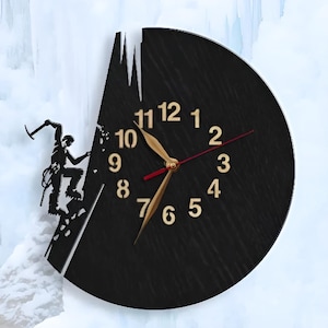 May include: Black clock with gold numbers and hands, featuring a silhouette of a climber scaling a rock face. The clock is shaped like a mountain with an icicle hanging from the top.