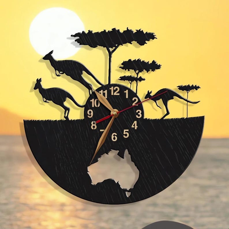 May include: Black wooden clock with a silhouette of kangaroos and trees. The clock face has a gold hour hand and a red minute hand. The clock is shaped like a half circle with a cutout of the continent of Australia in the center.