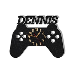 May include: Black wooden game controller clock with the name "DENNIS" above the clock face. The clock face has gold numbers and hands.