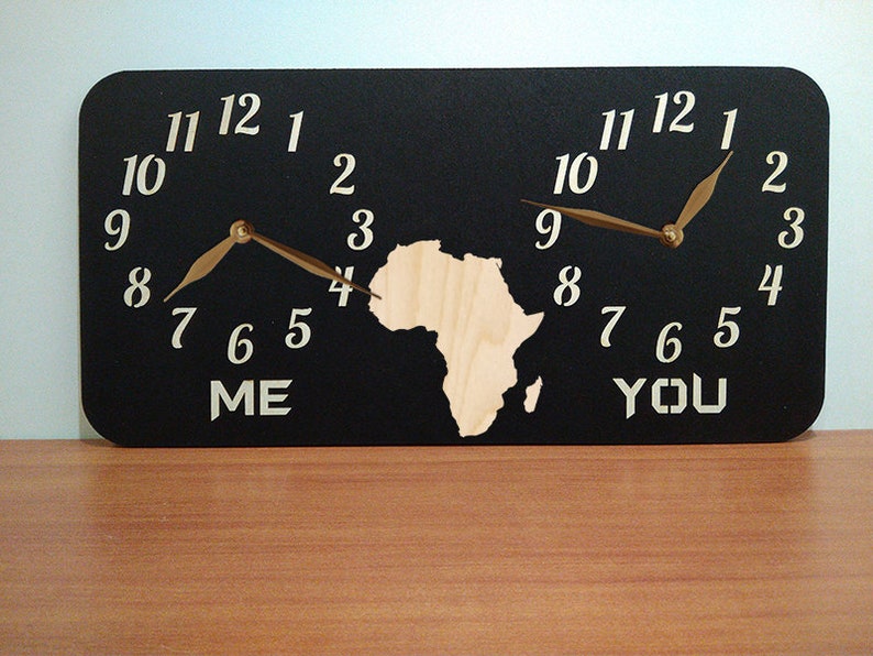 May include: A black wooden clock with two clock faces, one labelled "ME" and the other labelled "YOU". The clock faces are separated by a cutout of the continent of Africa. The clock hands are gold.