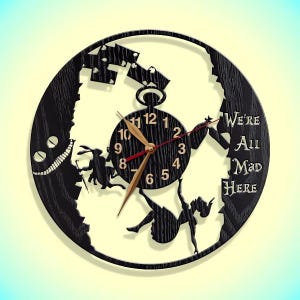 May include: Black wooden clock with a silhouette of Alice falling down a rabbit hole. The clock face features Roman numerals and the text "We're All Mad Here".