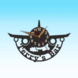 May include: Black airplane-shaped wall clock with gold hands and numbers. The clock has a white cloud design and the text "Terry's Bar" around the edge.