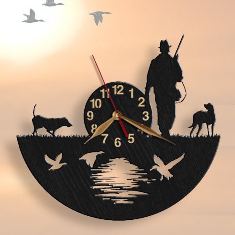 May include: Black wooden clock with a silhouette of a hunter, two dogs, and ducks. The clock face has gold numbers and hands. The background is a sunset scene.