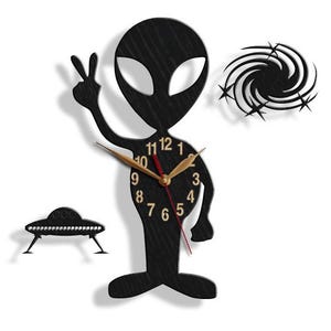 May include: Black alien clock with a gold clock face and red hands. The alien is holding a peace sign with its left hand and has a swirling galaxy design behind it.