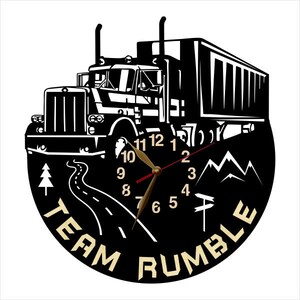 May include: Black and white clock featuring a semi-truck design. The clock face includes a road, mountains, and trees. The clock hands are red and gold. The clock face reads "Team Rumble".