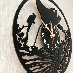 May include: Black wooden wall clock with a silhouette of a person diving into the ocean. The clock face has gold numbers and hands.