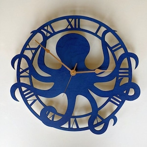 May include: A blue wooden wall clock with an octopus design. The clock face features Roman numerals and copper-coloured hands. The octopus is central within a circular frame.