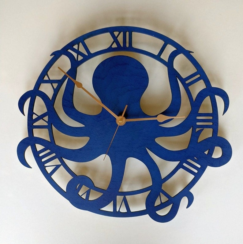 May include: A blue wooden wall clock with an octopus design. The clock face features Roman numerals and copper-coloured hands. The octopus is central within a circular frame.