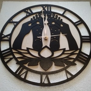 May include: A black and white wooden clock with Roman numerals. The clock face features a lotus flower and two feet in a yoga pose.