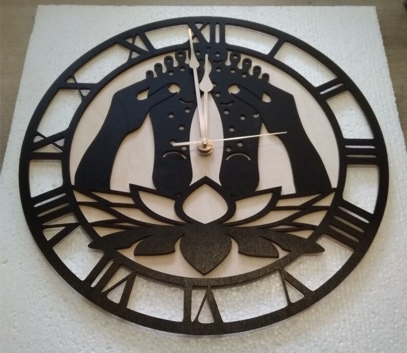May include: A black and white wooden clock with Roman numerals. The clock face features a lotus flower and two feet in a yoga pose.