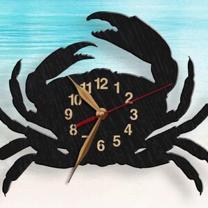 May include: A black wall clock shaped like a crab with a textured surface. The clock face features gold-colored numbers from 1 to 12, two gold-colored hour and minute hands, and a thin red second hand centered on the crab's body.