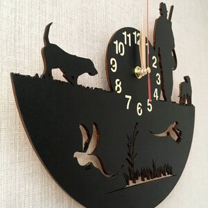 May include: Black wooden clock with a hunter, two dogs, and birds in flight. The clock face has gold numbers and hands.