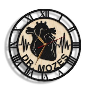 Pode incluir: Rel&oacute;gio em forma de cora&ccedil;&atilde;o preto e branco com moldura preta e numerais romanos. O mostrador do rel&oacute;gio &eacute; de madeira e apresenta um gr&aacute;fico de batimento card&iacute;aco e o texto "DR. MOZES".