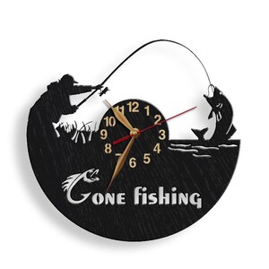 May include: Black and white wall clock with a silhouette of a fisherman casting a line and a fish jumping out of the water. The clock face has gold numbers and hands. The text "Gone Fishing" is printed below the clock face.