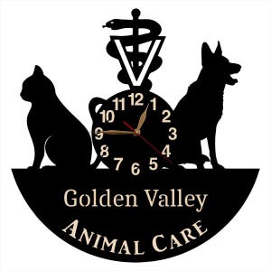May include: Black vinyl record clock with a silhouette of a cat, dog, and a caduceus symbol. The clock face has gold numbers and hands. The text "Golden Valley Animal Care" is printed below the clock face.