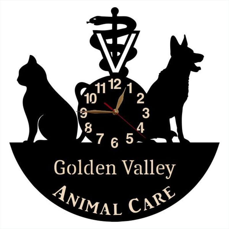 May include: Black vinyl record clock with a silhouette of a cat, dog, and a caduceus symbol. The clock face has gold numbers and hands. The text "Golden Valley Animal Care" is printed below the clock face.