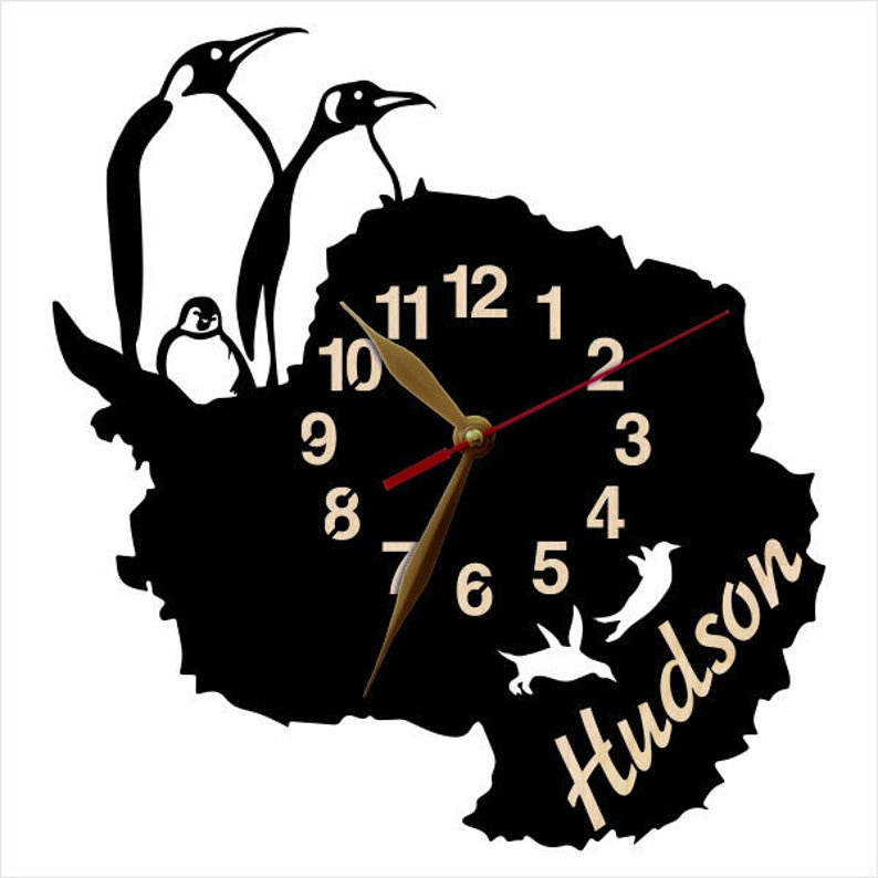 May include: Black and white silhouette of penguins and a clock face with gold hands and Roman numerals. The clock face is shaped like the continent of Antarctica. The text "Hudson" is written in a cursive font below the clock face.