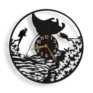 May include: Black and white wall clock with a silhouette of a manta ray and two scuba divers. The clock face has gold numbers and hands.